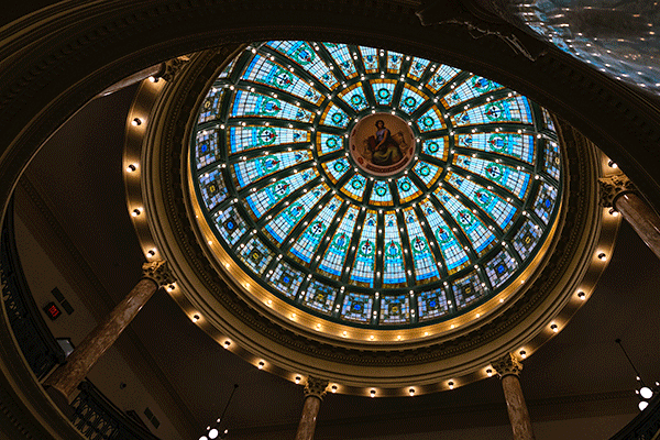 A large, colorful and intricate dome is illuminated in the ceiling of a large open space in Normal Hall.